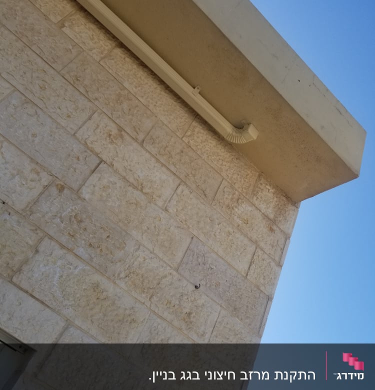 מרזב לבן מחובר לגג בטון על קיר אבן